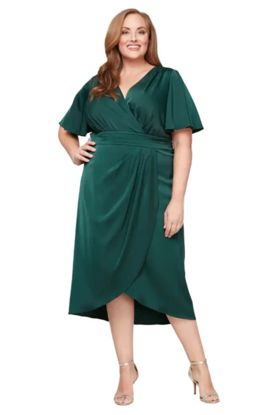 A woman wearing a green wrap dress with short sleeves, standing and smiling.